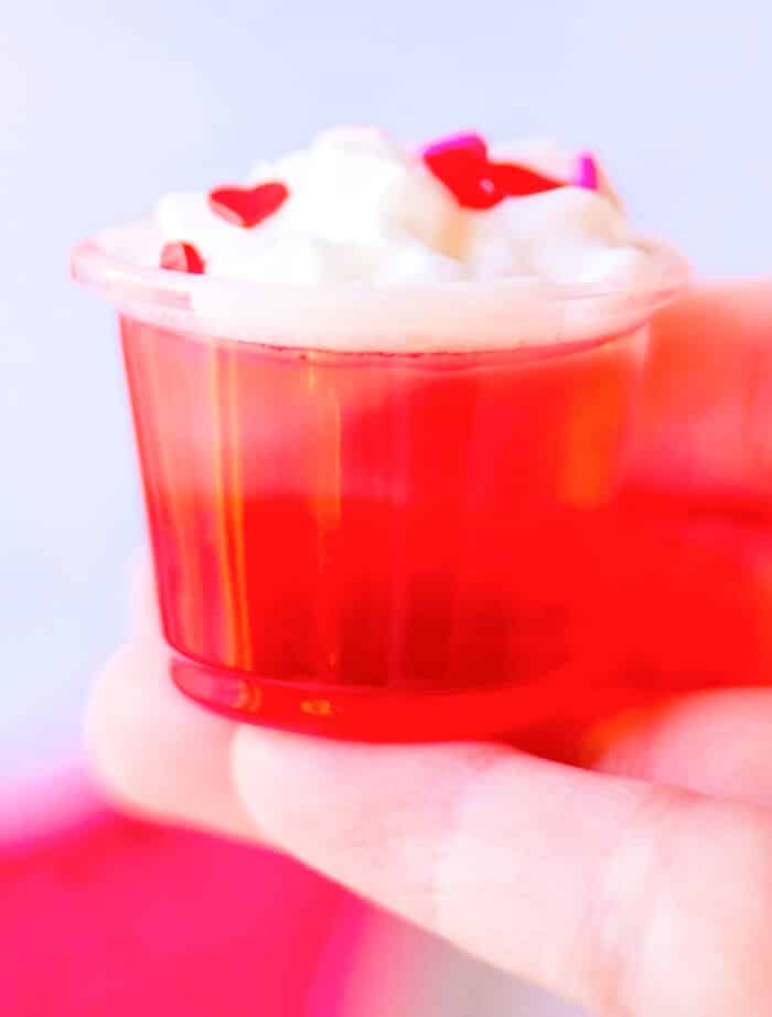 Valentine’s jello shots are a festive layered shot of raspberry and strawberry jello topped with whipped cream & sprinkles! RED JELLO SHOTS